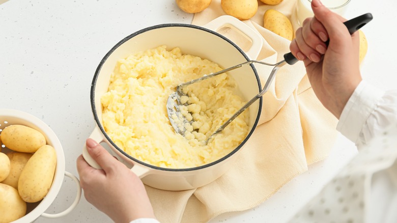 A hand masher mashing potatoes