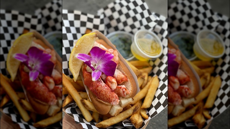 Lobster roll topped with floral garnish and a lemon slice, served with fries and butter