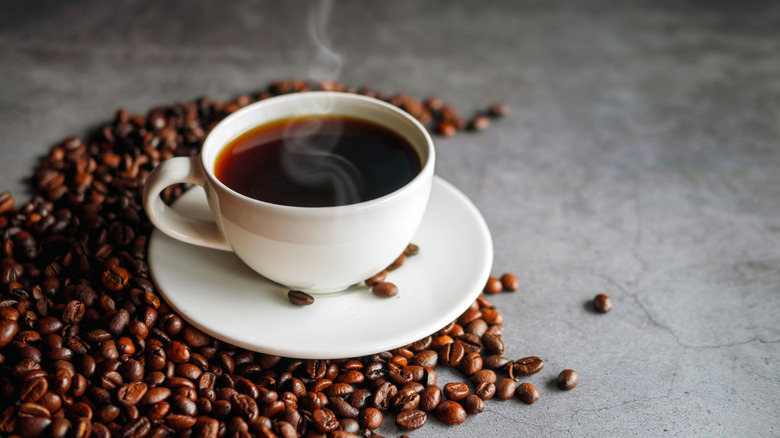 Coffee in a small white cup on saucer surrounded by coffee beans