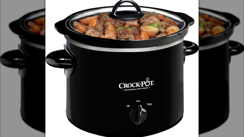 small, black Crock-Pot on white background filled with veggies, diced meat, and potatoes