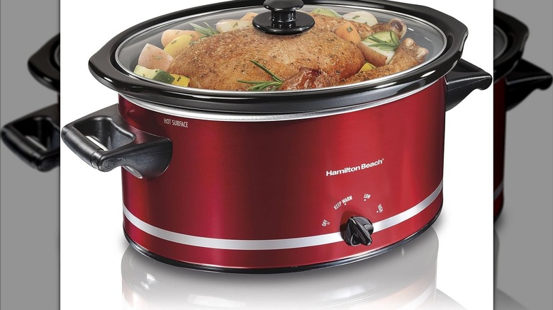 shiny red Hamilton Beach slow cooker with large piece of meat and veggies inside