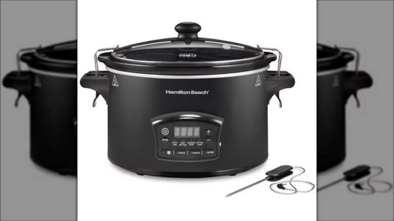 large black slow cooker with digital interface next to meat thermometer on white background