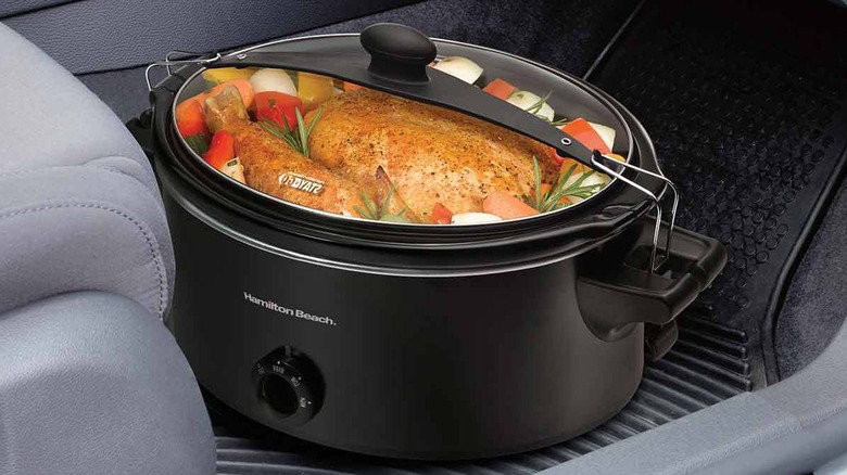 sleek black slow cooker carrying poultry and vegetables on the floor of car interior