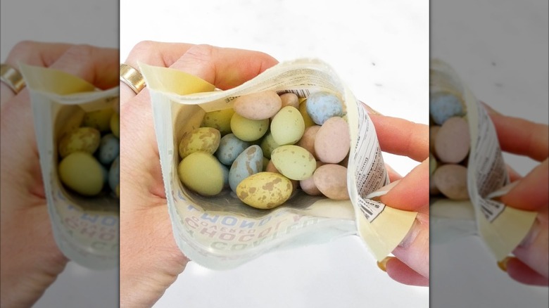 hands holding a bag full of candy coated dark chocolate almonds in many colors