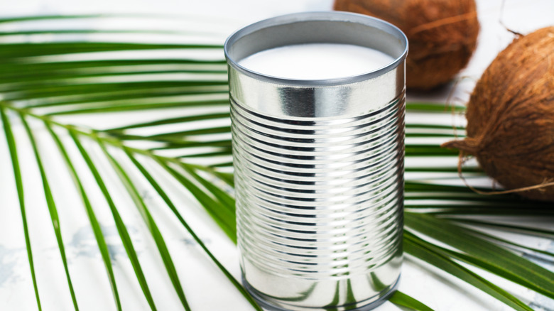 Opened can of coconut milk with fresh coconuts and palm leaf