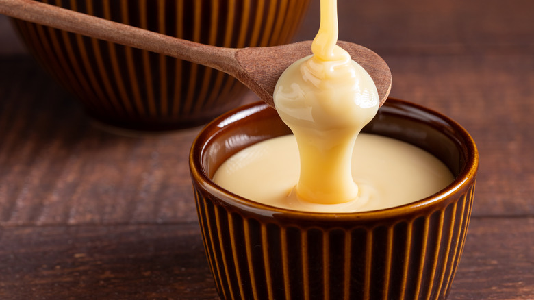 Pouring condensed milk into bowl over wooden spoon