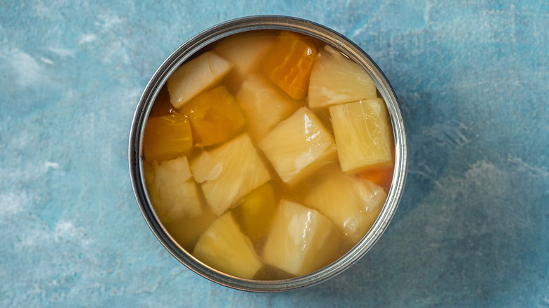 Opened can of pineapple chunks on blue background