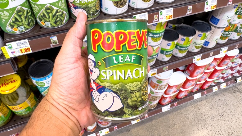 Hand holding can of spinach in grocery store