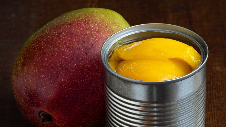 Mango slices in can next to whole fresh mango