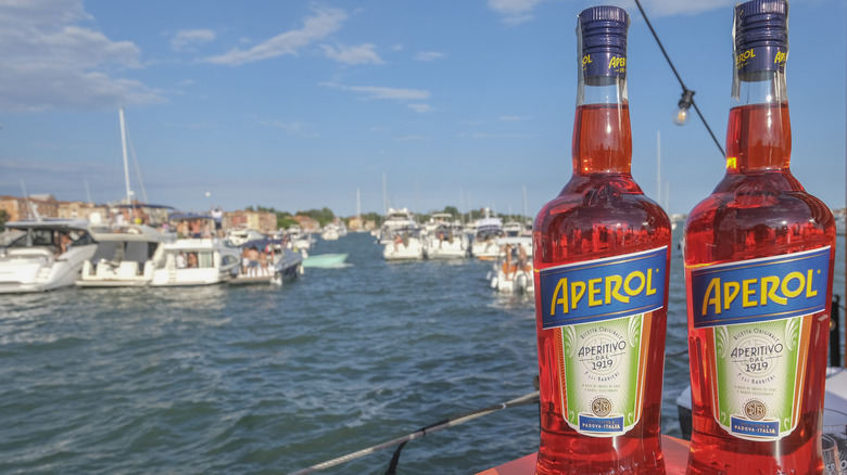 Two bottles of Aperol with boats in water in background