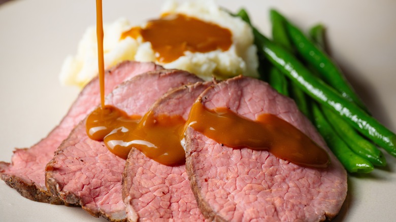 Gravy being poured onto roast beef slices