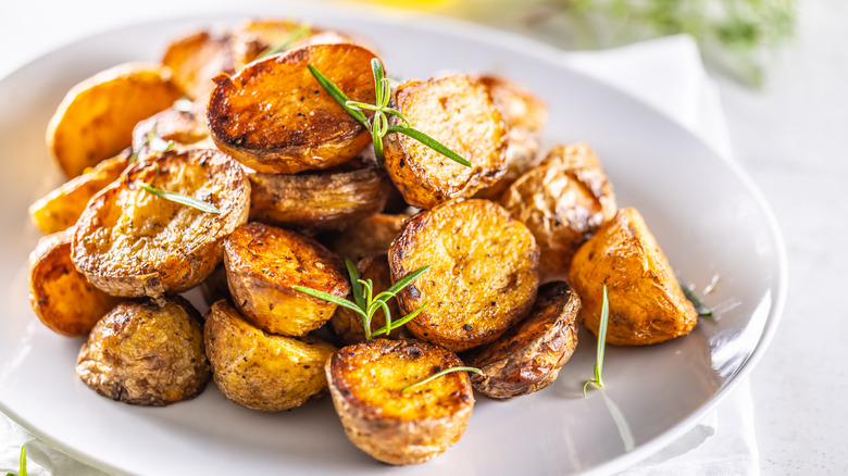 Pile of roasted potatoes on plate with rosemary garnish
