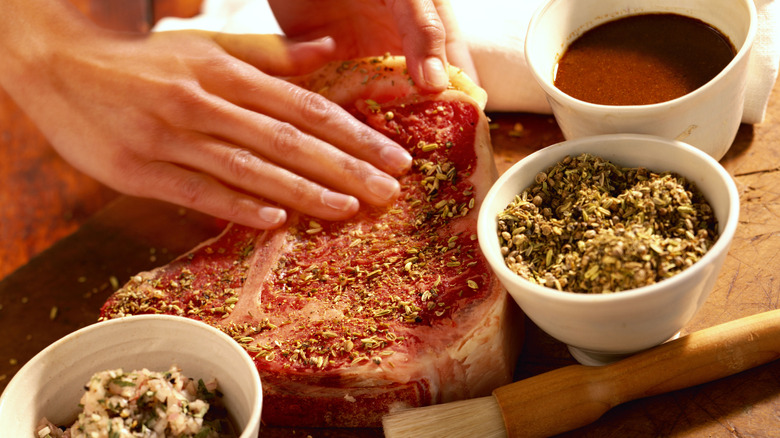Person marinating steak with herbs and dressing