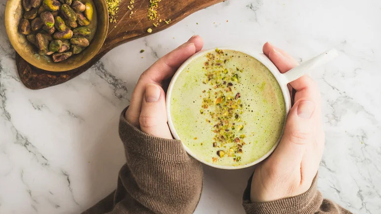Hands holding DIY deluxe pistachio latte on white countertop