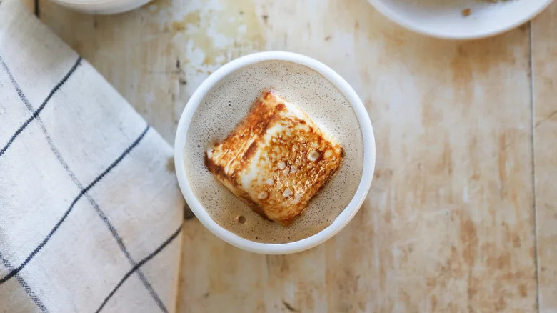 Vegan campfire s'mores latte in white cup on wooden table with napkin