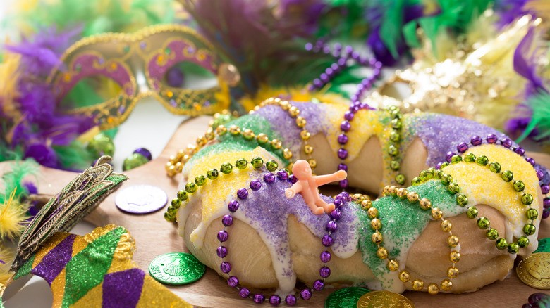 Plastic baby sitting on cake with Mardi Gras beads and coins