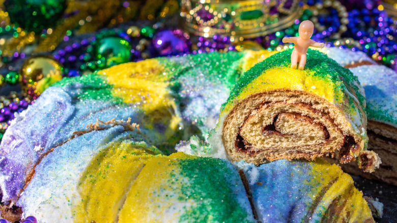 Cinnamon swirl filling inside of a decorated king cake with plastic baby sitting on top