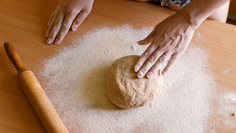 person working with flour and dough blob on a table with rolling pin