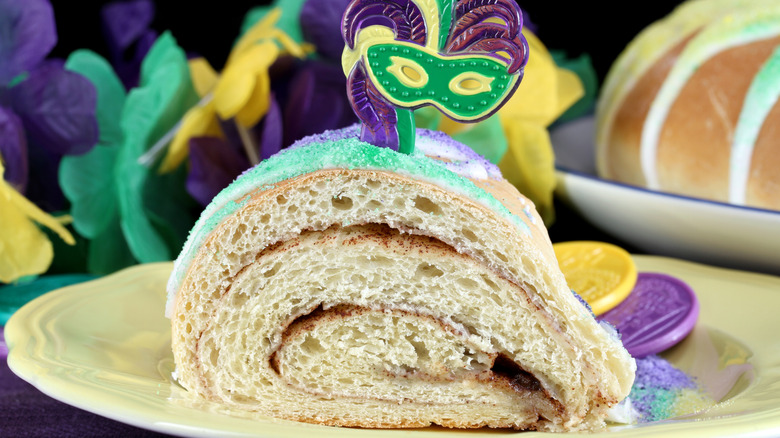 Slice of king cake on plate with plastic decorative mardi gras mask