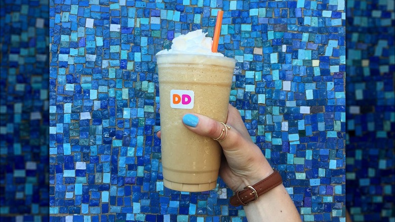 Hand holding a Dunkin' Coffee Coolatta blue mosaic background