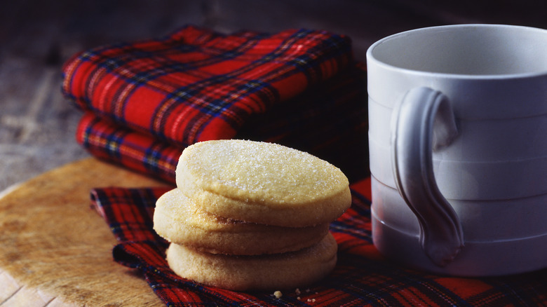 Round shortbread cookies on a tablecloth and next to a mug