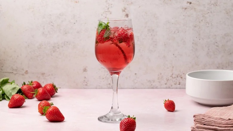 strawberry and basil wine spritzer in wine glass with fresh strawberries and basil leaves scattered on the counter