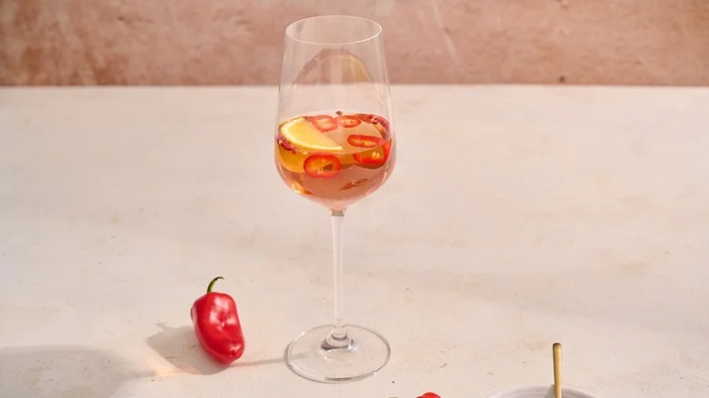 Rosé in a tall wine glass with chiles inside the glass and a whole chile on the table beside the glass