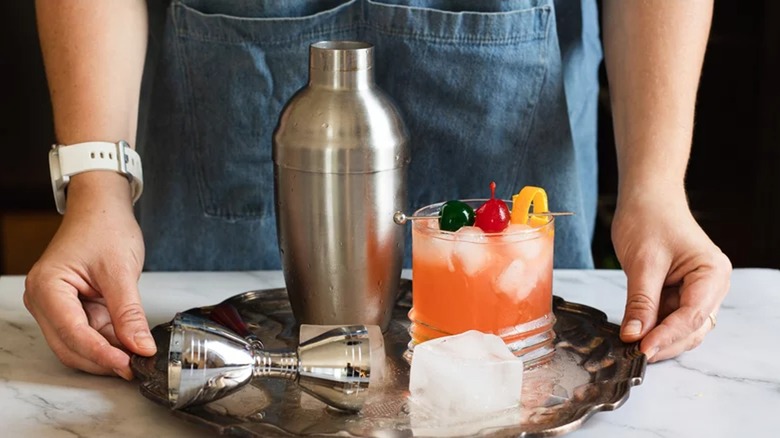 image of waiter placing down a sex on the beach cocktail with a cocktail shaker and ice cube next to it