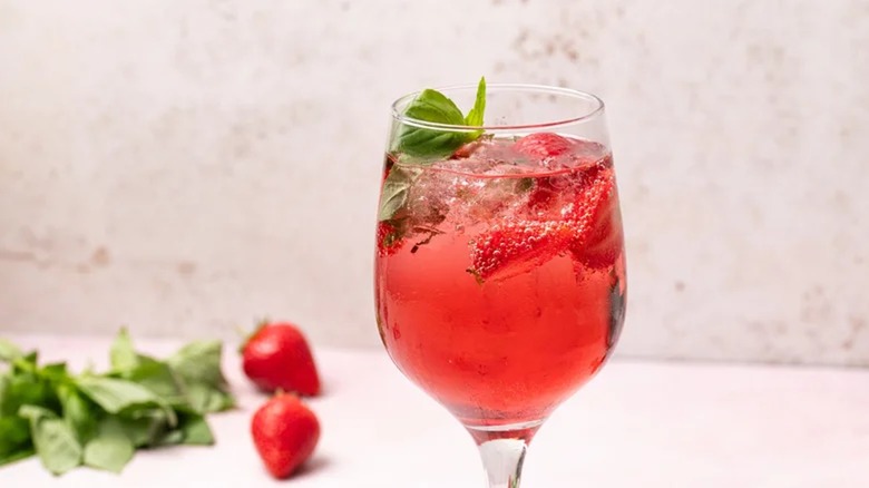 strawberry and basil wine spritzer in wine glass with basil and strawberries on table in background