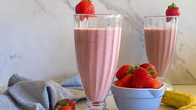 two strawberry smoothies in tall glasses with fresh strawberries on the side