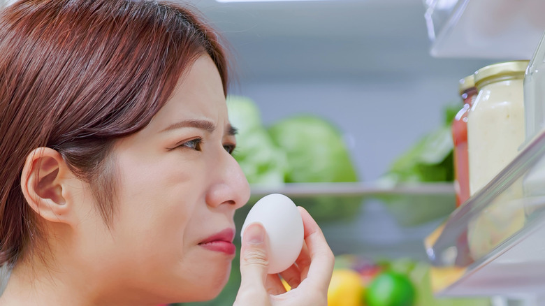 Woman smelling egg from refrigerator