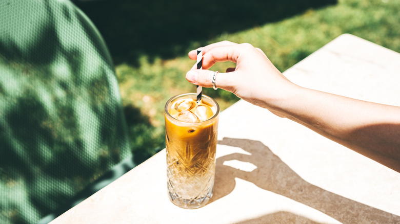 An iced tea on a table being stirred with black and white striped straw