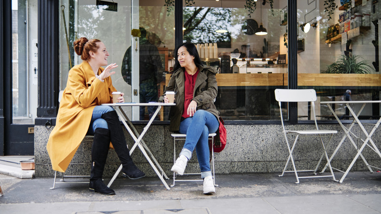 Two friends drinking coffee at a small table outside a coffee shop