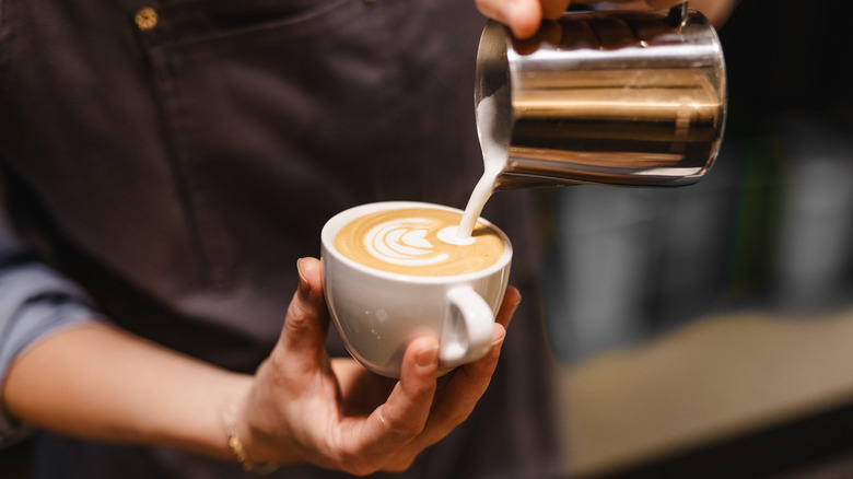 A barista making coffee art with a jug of milk