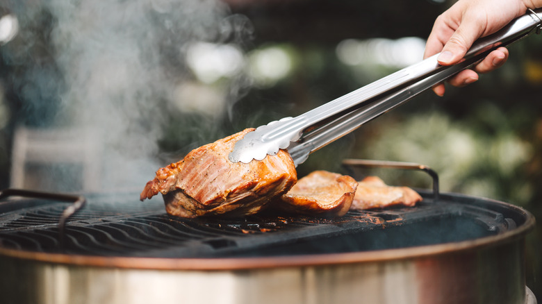 Person grilling meat with tongs