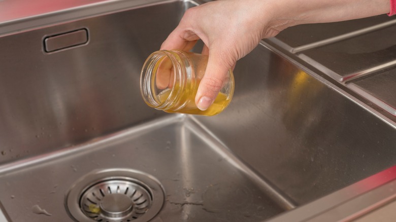 Hand pouring oil down drain