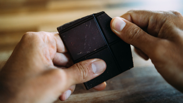 Hands holding dark chocolate piece