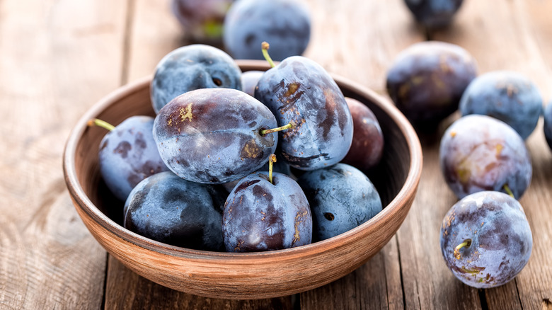 Purple plums in a wooden bowl