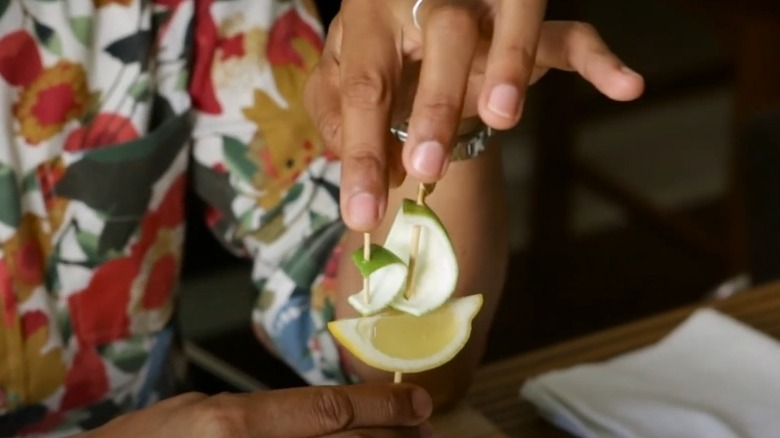 Making a boat-shaped cocktail garnish with a lemon wedge, lime peel, and wooden skewers