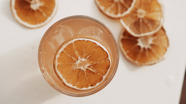 Top-view of an orange cocktail garnished with a dry orange slice floating on top, surrounded by four dry orange slices