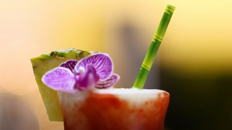 a close-up of the top of tiki cocktail garnished with an orchid and a green faux bamboo straw