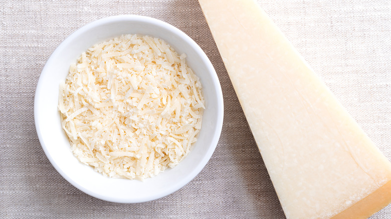 Grated Parmesan cheese in bowl next to wedge of cheese