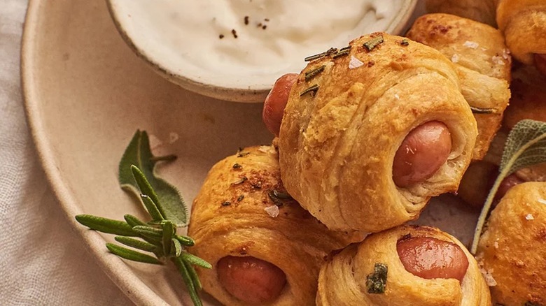 herby pigs in a blanket displayed on a plate with dipping sauce