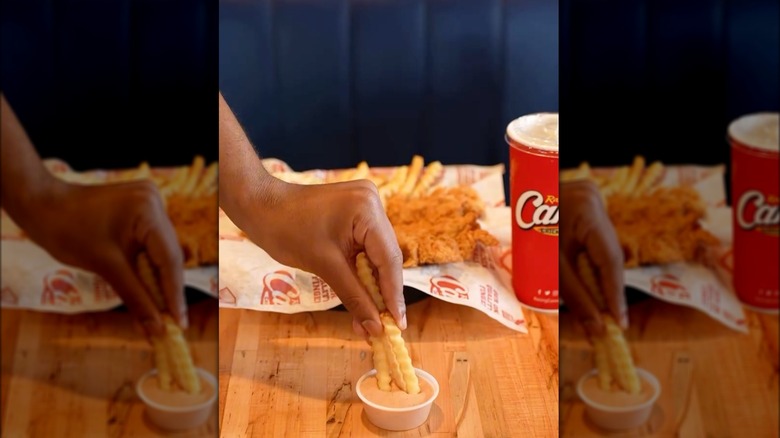 A person is dipping fries into Raising Cane's sauce