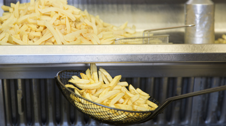 Ladle holding fresh french fries out of the fryer