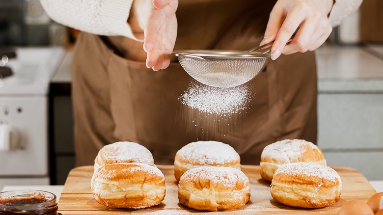 Sprinkling powdered sugar over donuts