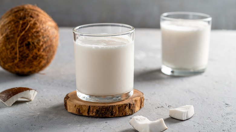 Two glasses of coconut milk with fresh coconut pieces in the foreground