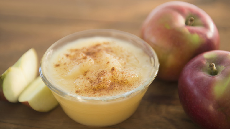 Cup of applesauce with cinnamon and red apples