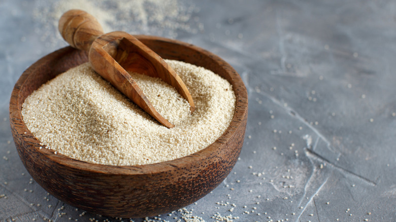 Raw fonio seeds in bowl with wooden scoop and grey background