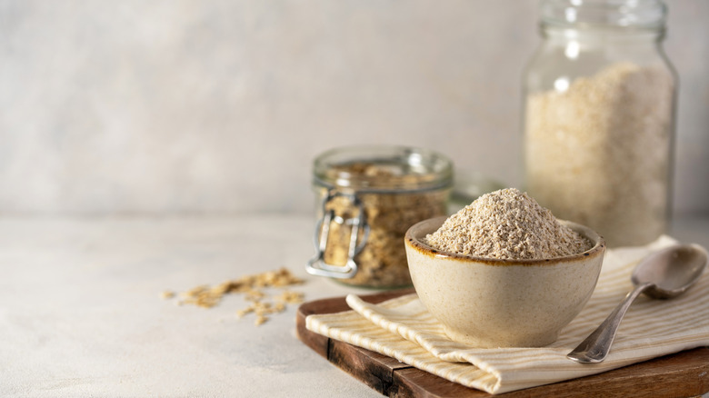 Bowl of oat flour with containers of oats and fabric towel